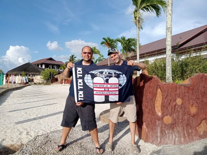 Jonathan Venn and Phil Jennings holding a TDI flag after completing the SDI Sidemount Instructor course in Moalboal, March 2023.